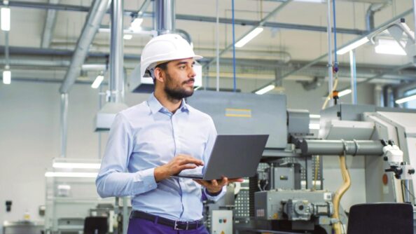 Mann in einer Produktionshalle mit Laptop in der Hand