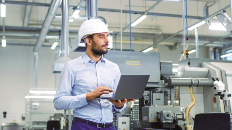 Mann in einer Produktionshalle mit Laptop in der Hand