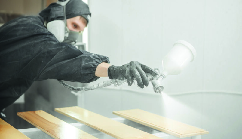 Industrielackierer beschichtet Bauteile aus Holz.